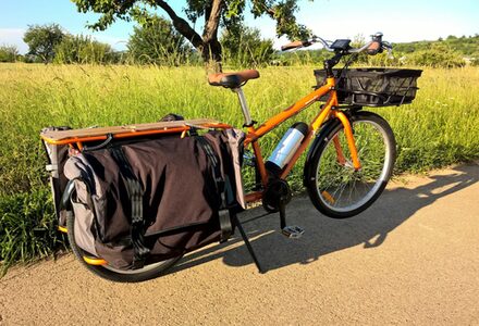 Ein Oranges Lastenrad mit einem sehr langen Gepäckträger um Kinder zu transportieren.